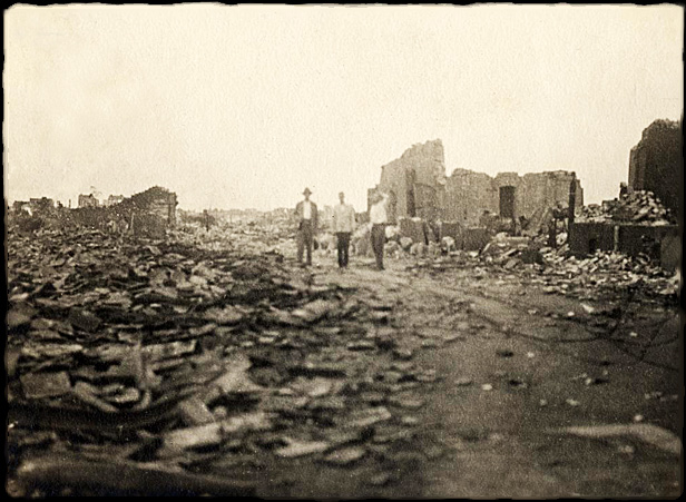 Three men from the Taiyo Maru, standing amidst ruins. Location in city unknown.